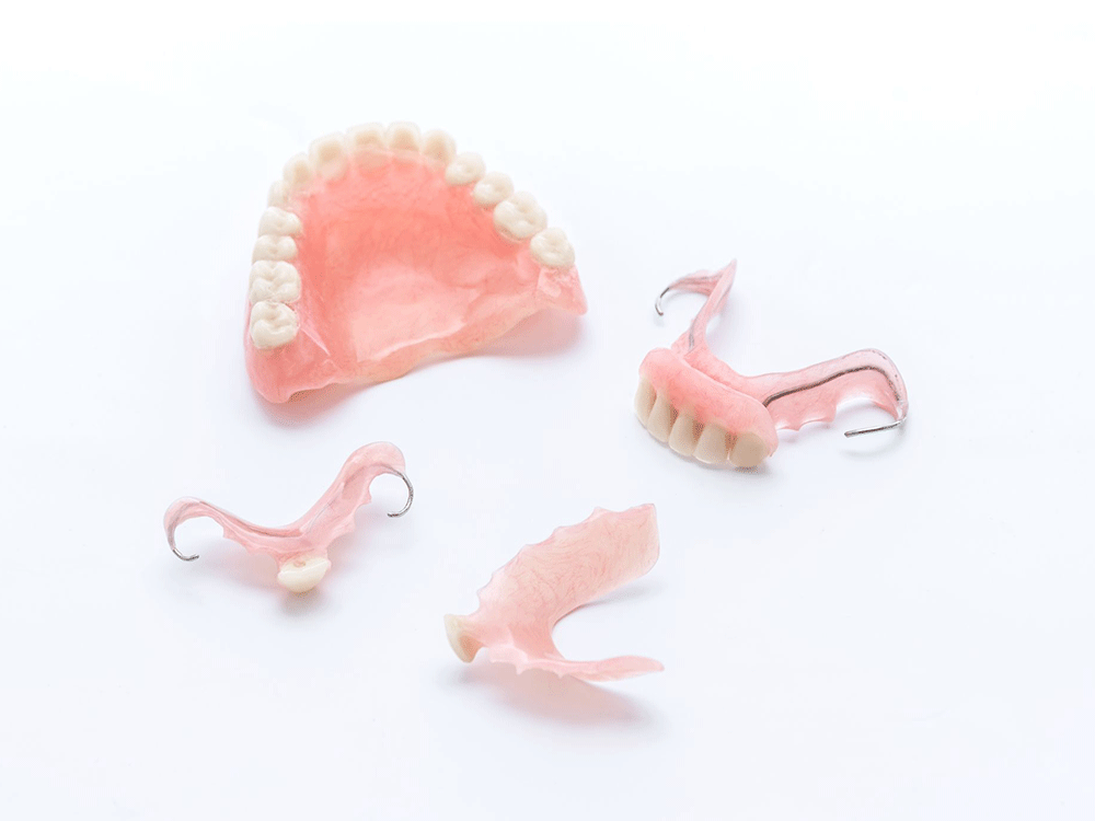 A collection of various types of dentures and partial dentures placed on a white background, showing different designs and configurations used to replace missing teeth and restore dental functionality.